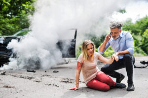 Young woman by the car after an accident in Orlando, FL and a man with smartphone, making a phone call.