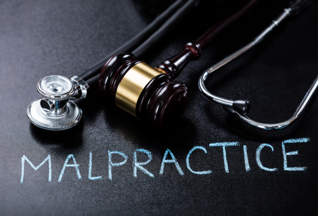 Stethoscope and gavel resting on a black surface with the word 'MALPRACTICE' written in chalk, symbolizing medical malpractice and legal action